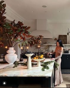 a woman standing in a kitchen next to a table with fruit and candles on it