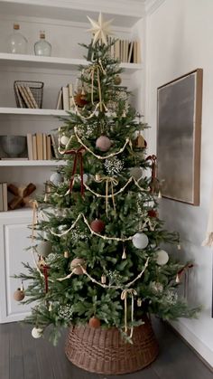 a small christmas tree in a wicker basket on the floor next to a bookshelf