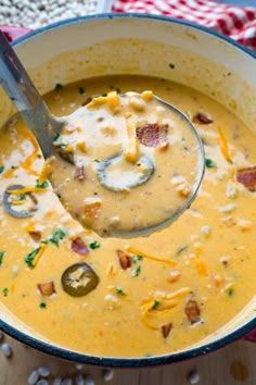 a ladle full of soup with cheese and bacon in it on a wooden table