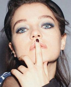 a woman with blue eyes is making a hush gesture to the camera while holding her finger in front of her mouth