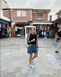 a woman standing in the middle of a street with people walking around and shops on both sides