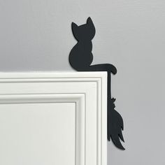 a black cat sitting on top of a white door frame next to a gray wall