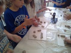 a group of kids standing around a table with rocks and paper on top of it