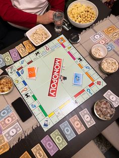 a monopoly board game on a table with bowls of cereal and plates of food around it