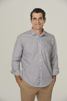 a man standing with his hands in his pockets and smiling at the camera he is wearing a blue checkered shirt