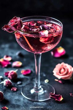 a close up of a drink in a wine glass with rose petals on the table