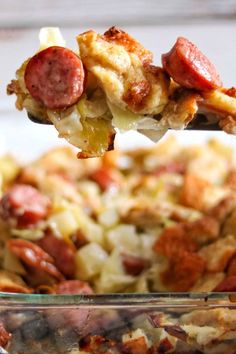 a spoonful of sausage and potato casserole is being lifted from the casserole dish