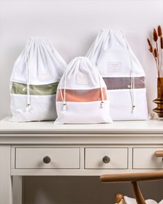 two white bags sitting on top of a table next to a wooden chair and vase