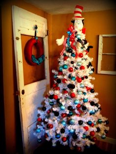 a white christmas tree with red, blue and green ornaments in front of an open door