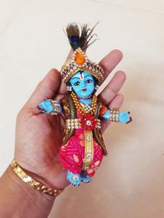 a hand holding a small blue and red doll in it's right hand,