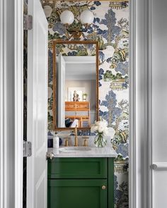 a bathroom with green cabinets and wallpaper on the walls, along with a gold framed mirror