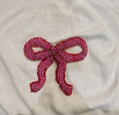 a pink bow on top of a white shirt that is made out of beads and thread