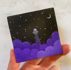 a hand holding up a small painting of a space station in the sky with clouds