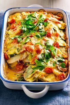 a casserole dish with vegetables and cheese in it on a blue towel next to two white bowls