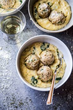 two bowls filled with meatballs and sauce next to a glass of wine on a table