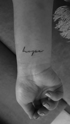 a woman's wrist with the word hope tattooed on her left arm, in black and white