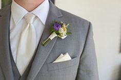 a man in a gray suit with a white tie and flower boutonniere