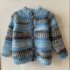 a crocheted blue and gray sweater hanging on a white hanger with buttons