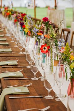 a long table is set up with wine glasses and flowers in vases on it