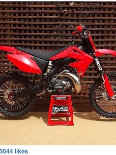 a red dirt bike sitting on top of a metal stand in front of a wooden fence