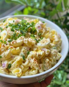 a white bowl filled with macaroni salad on top of a table next to green leaves