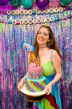 a woman holding a birthday cake in front of a backdrop