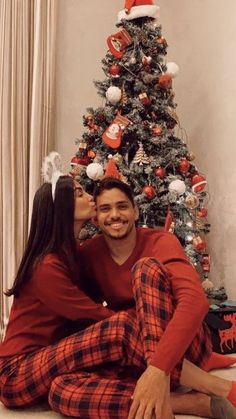 a man and woman sitting in front of a christmas tree wearing matching pjss