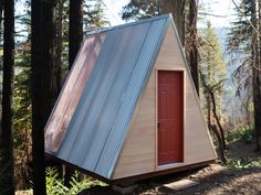 a small cabin in the woods with a red door and metal roof on it's side