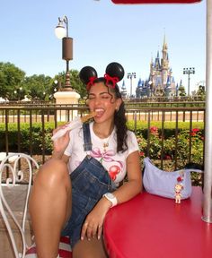 a woman sitting at a red table with minnie mouse ears on her head eating food