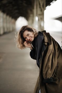 a woman leaning against a wall talking on her cell phone while wearing a trench coat