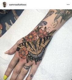 a woman's hand with a butterfly and flowers tattoo on it