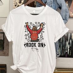 Rock On T-Shirt, Rocker shirt, Rodeo fan gear, Rodeo Kids, Brahman Darlin, NFR Fashion, NFR Afterparty, NFR number on back shirt, Buckle Bunny tee Thank you for shopping my small business. Please message me if you have questions. This is a physical shirt that is made when you order it and shipped out to you. If you love the design and would like it on a different type of item, rather message me and I will do what I can to get a different product to you. Shipping times are 2-5 days, but the longe Summer Rock T-shirt With Band Logo, Punk Graphic Print Top For Music Festival, Punk Style Tops With Graphic Print For Music Festival, Grunge T-shirt For Fall Music Festival, Punk Style Graphic T-shirt For Fall, Rock And Roll Short Sleeve T-shirt For Concert, Rock Style Band Logo T-shirt For Summer, Rock And Roll Style T-shirt For Summer Streetwear, Rock Style Crew Neck T-shirt For Music Festival