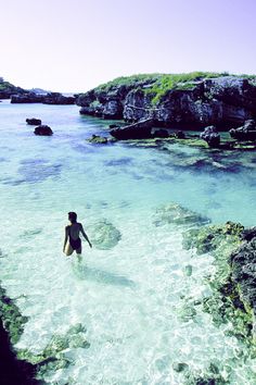 a man is wading in the clear blue water near some rocks and green plants