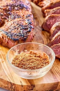 steak seasoning in a glass bowl on top of a cutting board next to meat