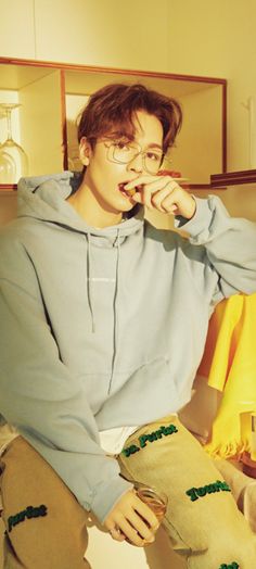 a young man sitting on top of a bed with his hands in his mouth and wearing glasses