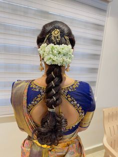 a woman with flowers in her hair wearing a blue and gold sari dress, looking out the window