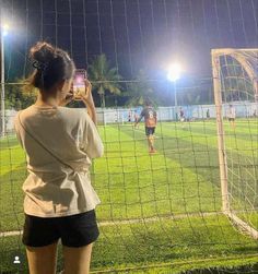 a woman standing in front of a soccer goal taking a photo with her cell phone