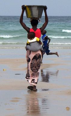 three people walking on the beach carrying items over their heads to the water's edge