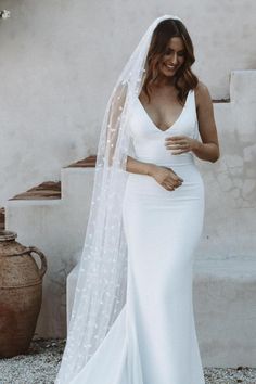 a woman in a white wedding dress and veil posing for the camera with her hand on her hip