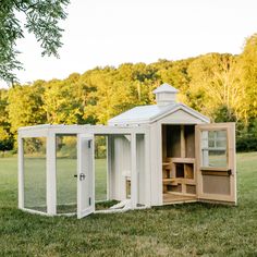 a chicken coop in the middle of a grassy field with trees in the back ground