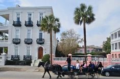 two horses pulling a carriage with people on it down the street in front of a large white building