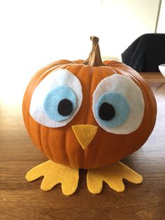 an orange pumpkin decorated with googly eyes and a yellow bird's beak is sitting on a wooden table