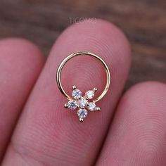 a person's finger with a gold nose ring and three small white stones on it