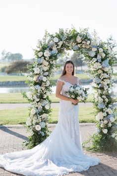 a woman in a wedding dress is standing under an arch with flowers on the side