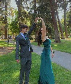 a young man and woman dressed in formal wear standing on grass with trees behind them