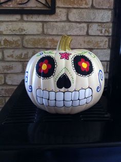 a white pumpkin decorated with sugar skulls and red eyes on a black shelf in front of a brick wall