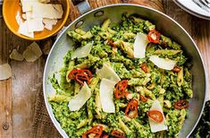 a pan filled with pesto and cheese on top of a wooden table next to utensils