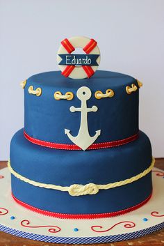 there is a blue cake with an anchor on top and red ribbon around the edges