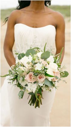 the bride is holding her bouquet on the beach