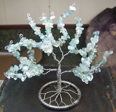 a wire tree with green and blue beads on it's branches is sitting on top of a piece of metal